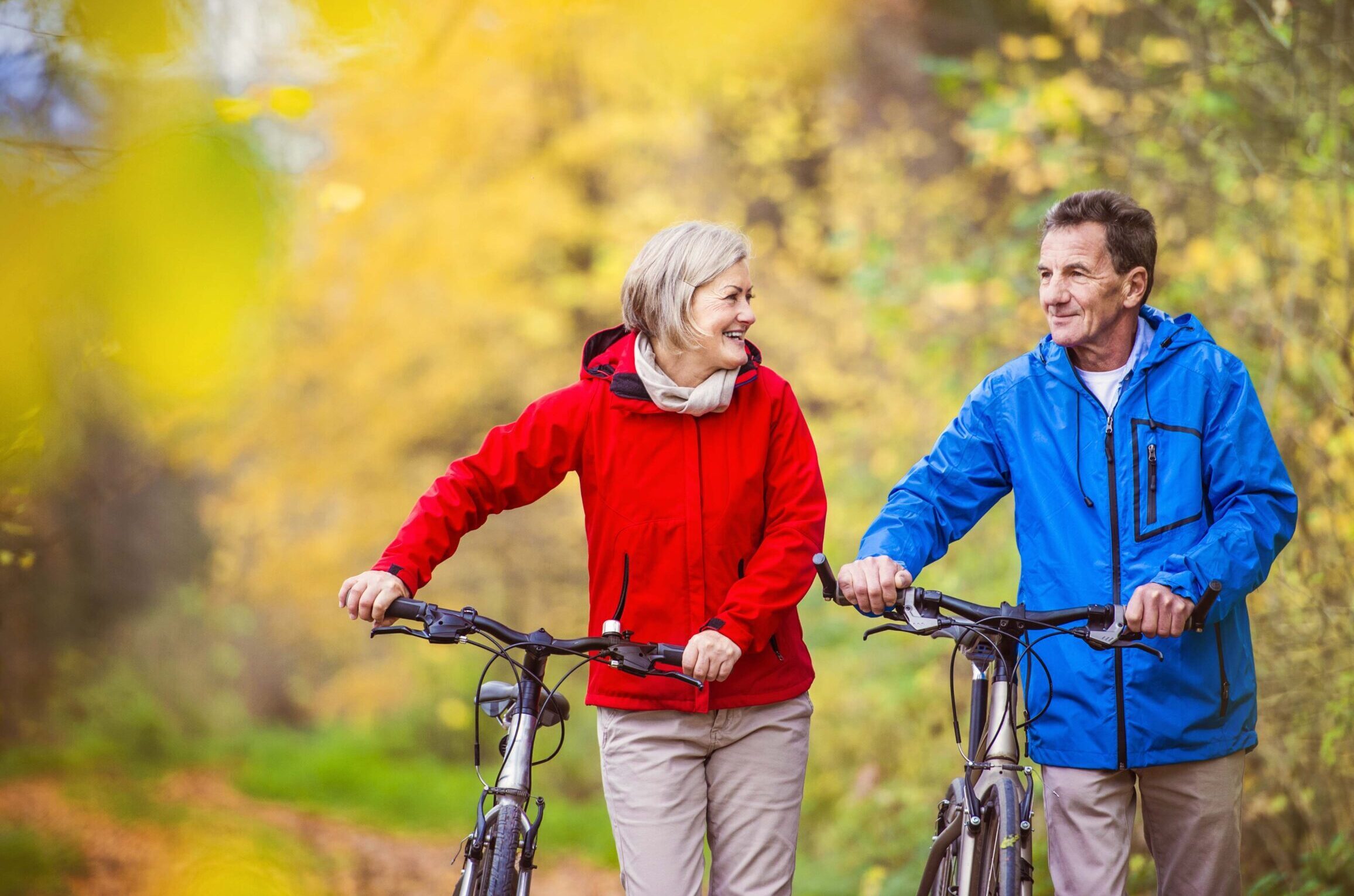 A senior couple walks with bikes through fall foliage.
