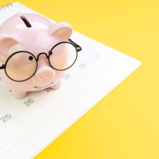 A piggy bank with glasses on sits on top of a calendar.
