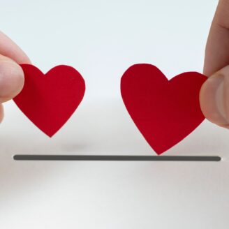 two hands drop small cut out paper hearts into a donation box opening