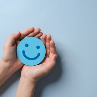 blue paper smiley face held out in open hands on a white background