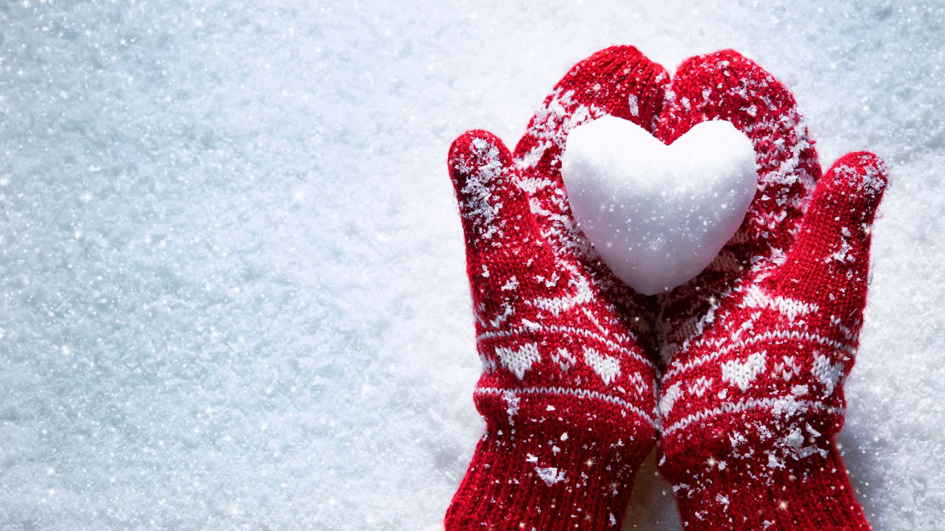 red mittens holding a heart shaped snowball in the snow