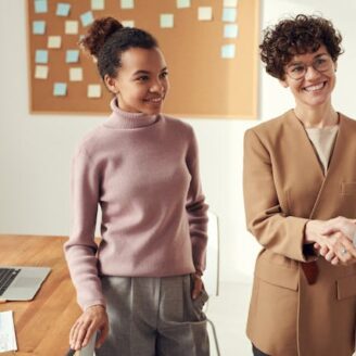 two women smiling one is shaking hands with a third woman. They are standing in an office